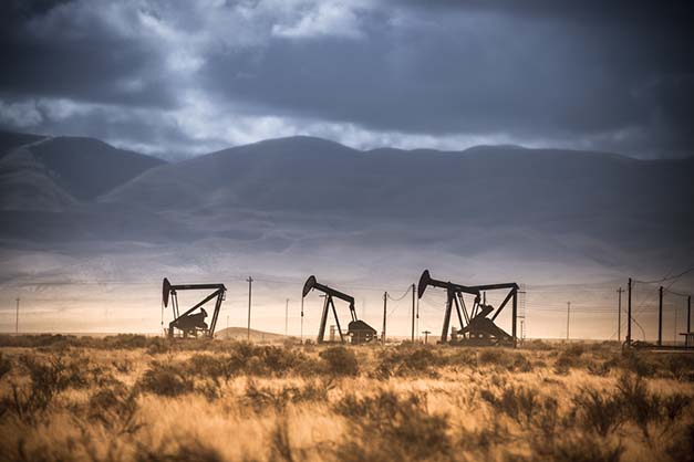 Pumpjacks lifts oil from a well. Muntains and dark clouds in the background.