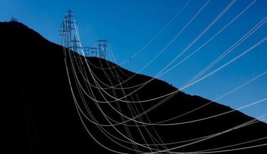 Electric transmission lines strung down black mountain against blue sky.