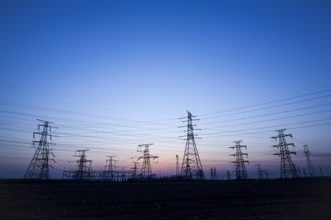 Several transmission towers with electricity wires silhouetted during sunset.