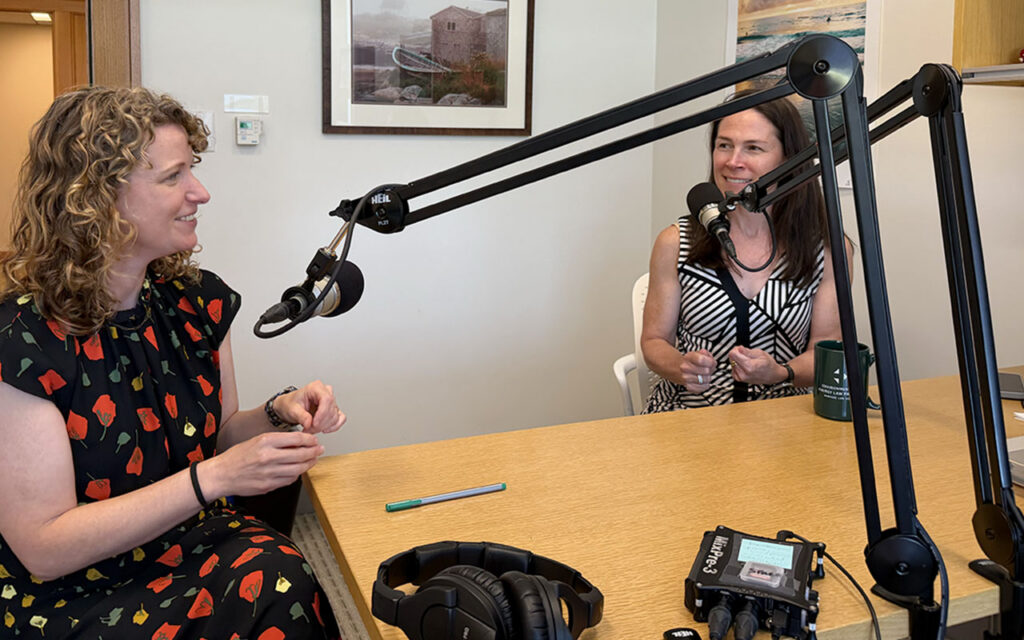 Two women talking into microphone and smiling.